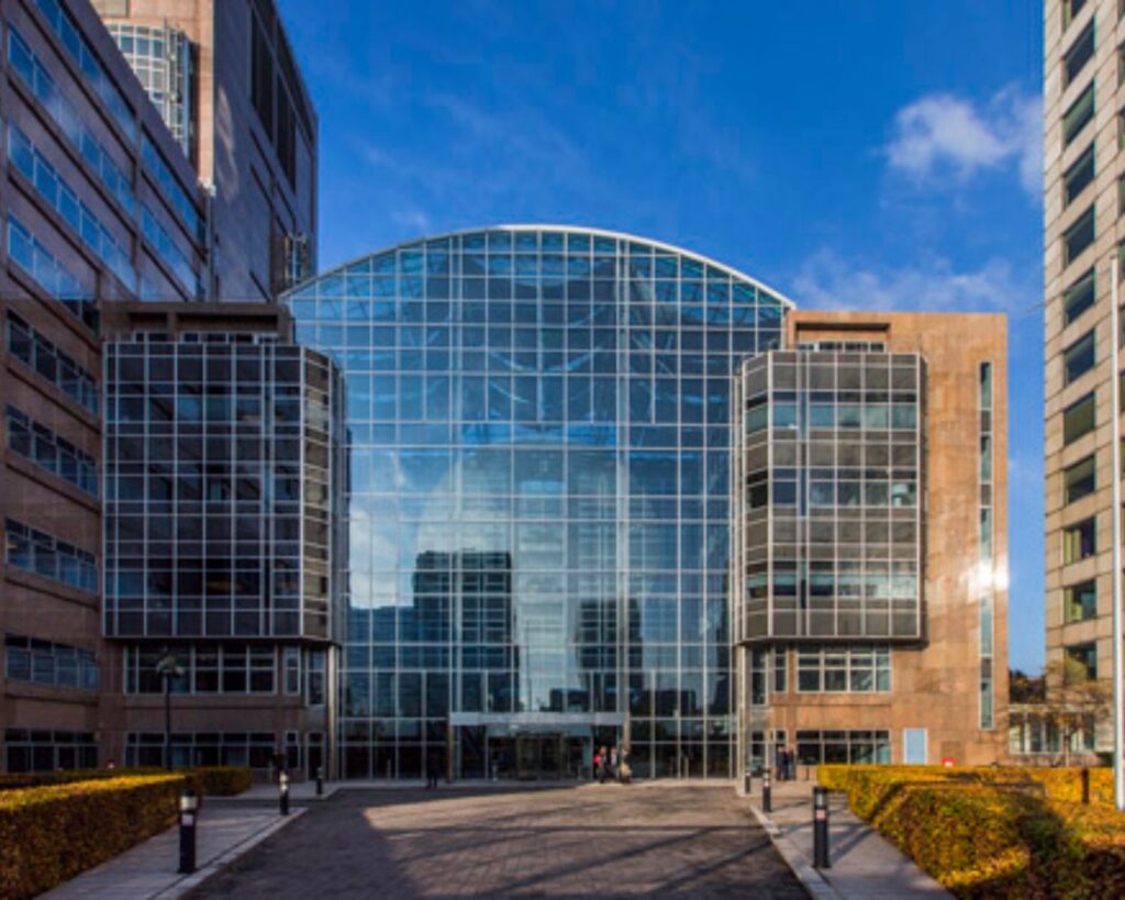 Modern kantoorgebouw met een opvallende glazen gevel en symmetrische architectuur, gefotografeerd onder een heldere blauwe lucht.