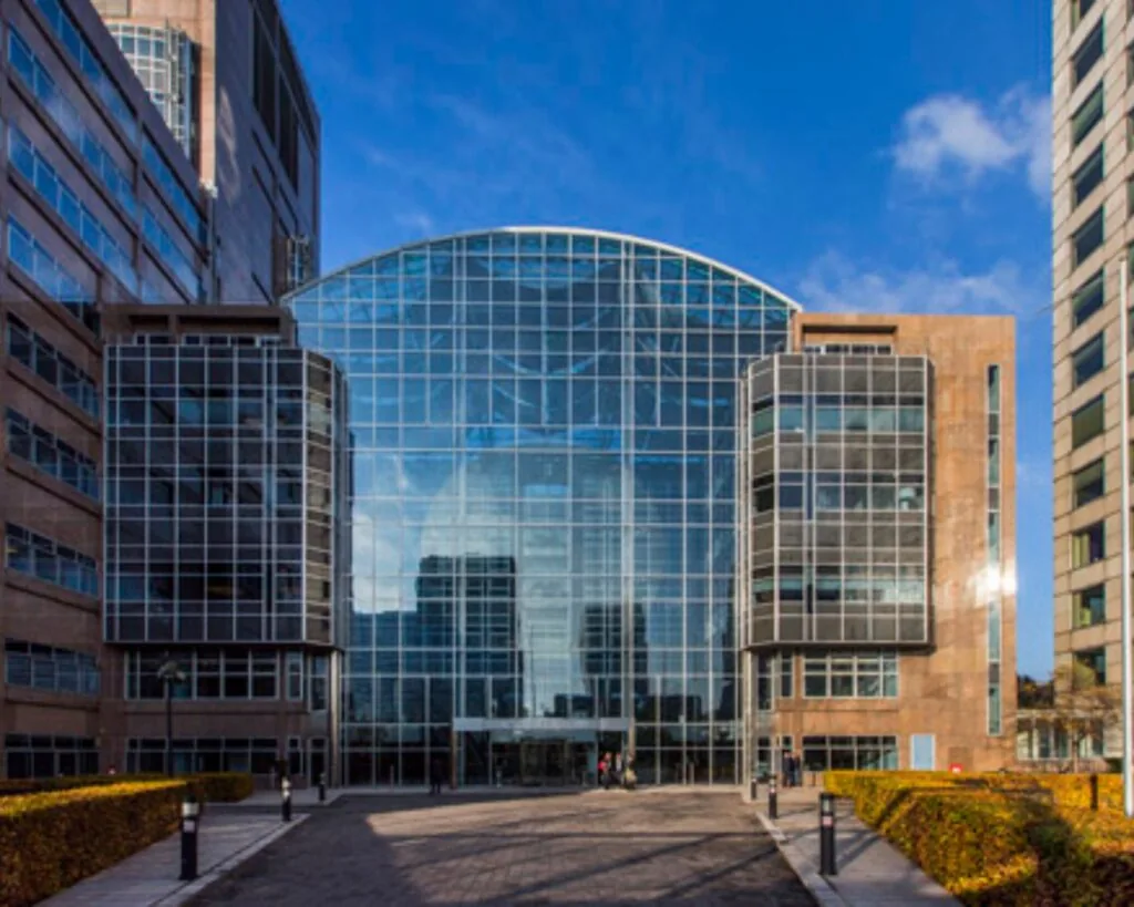 Modern kantoorgebouw met een opvallende glazen gevel en symmetrische architectuur, gefotografeerd onder een heldere blauwe lucht.