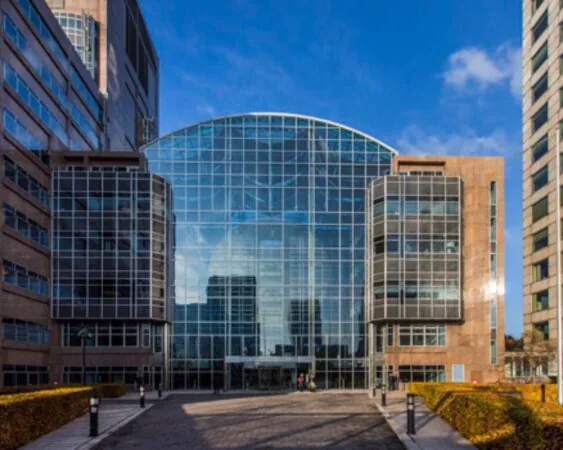 Modern kantoorgebouw met een opvallende glazen gevel en symmetrische architectuur, gefotografeerd onder een heldere blauwe lucht.