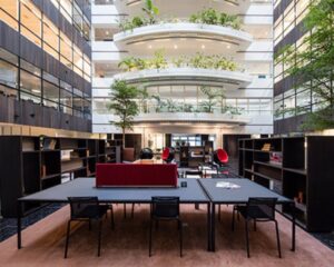 Moderne, open kantoortuin met veel groen, omgeven door meerdere verdiepingen met glazen balustrades.