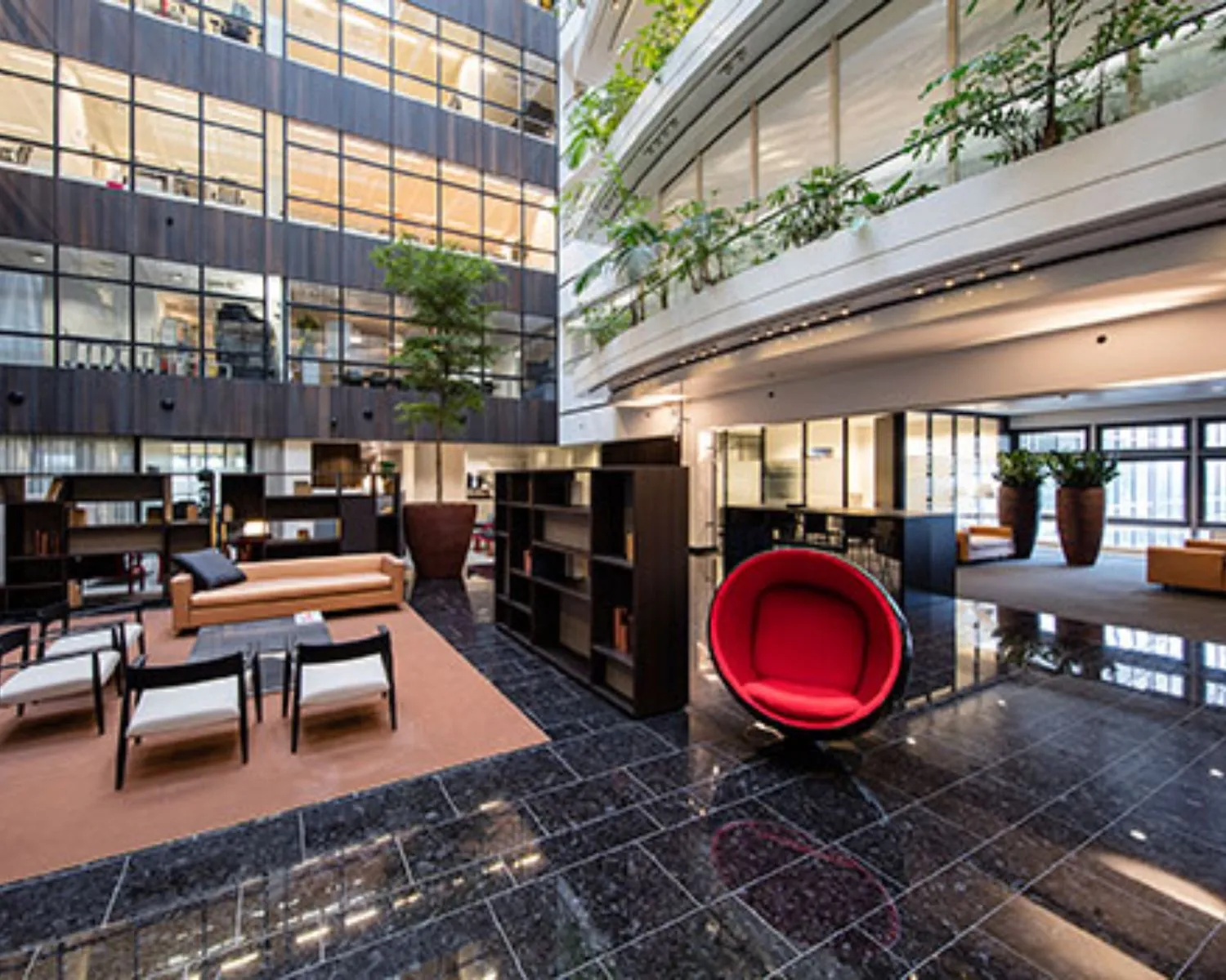 Moderne en ruime kantoorlobby met designmeubilair, grote planten en glazen gevels.