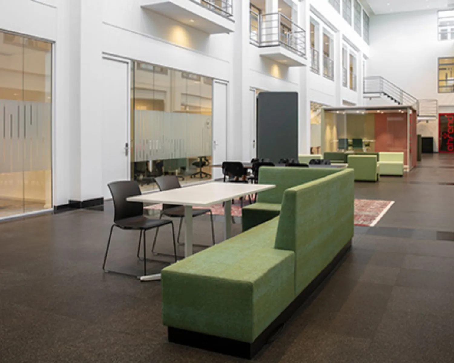 Moderne kantoorruimte met zithoeken, bureaus en glazen wanden in een open, licht atrium.