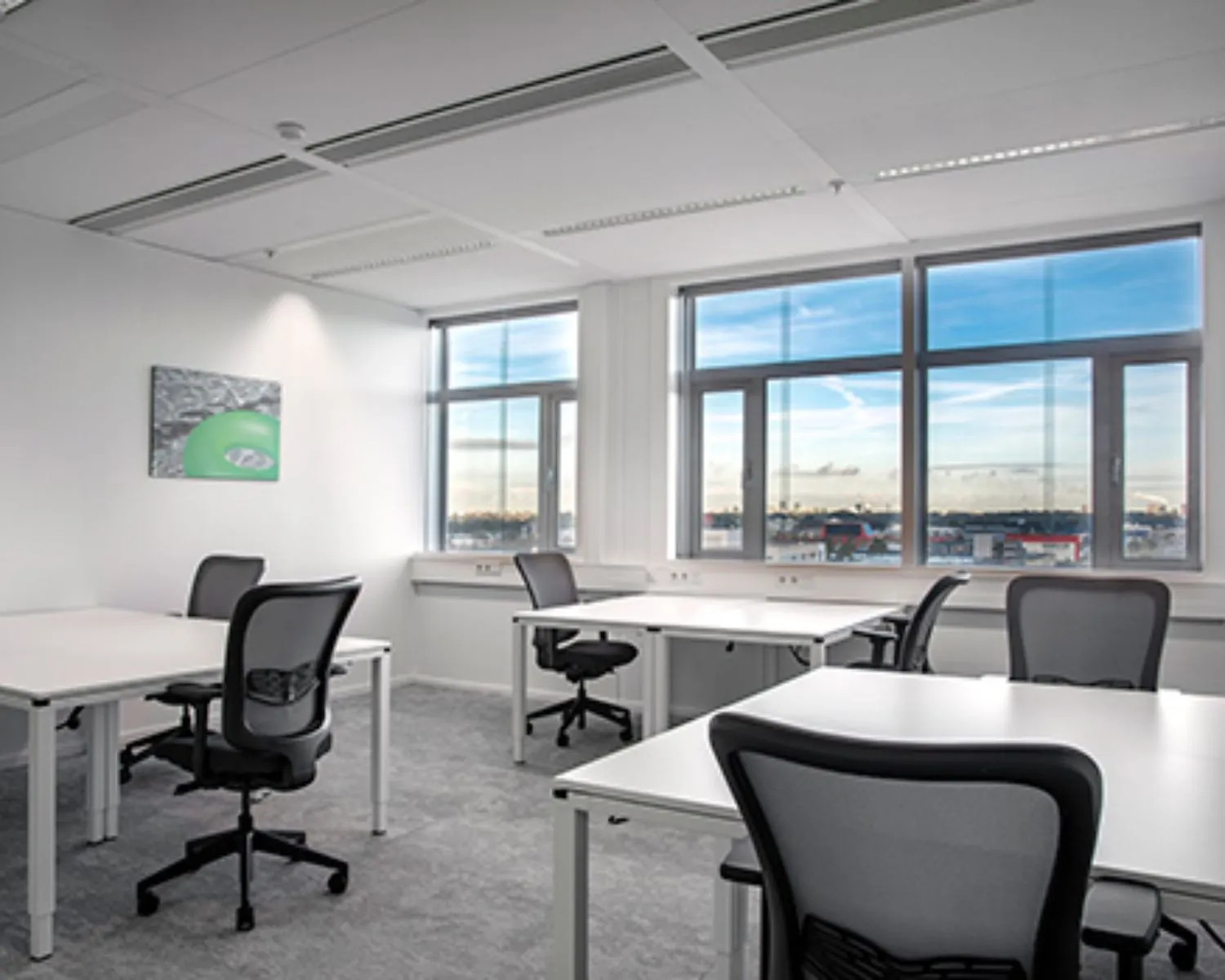 Moderne, lichte kantoorruimte met meerdere werkplekken en grote ramen met uitzicht op de stad.