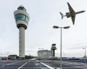 Een vliegtuig vliegt over de verkeerstoren en terminal van luchthaven Schiphol.