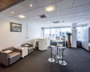 Moderne en lichte kantoorlounge met zitgedeelte, ronde statafel en uitzicht op een stedelijke skyline.