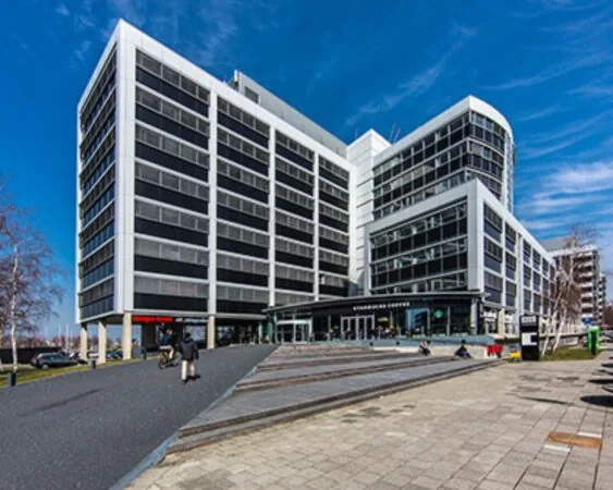 Modern kantoorgebouw met een Starbucks-filiaal op de begane grond en mensen op het plein ervoor.