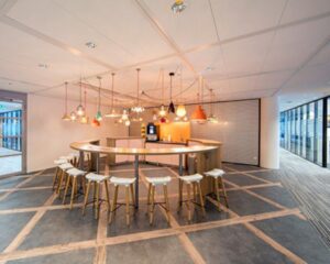 Moderne kantoor pantry met ronde bar, hoge barkrukken en een cluster van hanglampen aan het plafond.