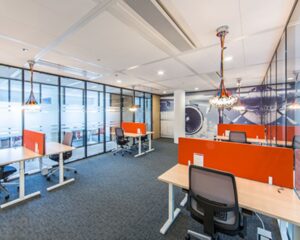 Modern kantoor met open werkplekken, oranje scheidingswanden en een luchtvaartthema op de muur.