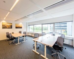 Moderne vergaderruimte met bureaus, bureaustoelen, grote ramen en wandfoto’s van vliegtuigen.