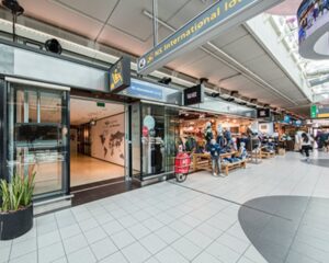 Ingang van de NS International Lounge op een druk winkelgebied in een station of luchthaven.