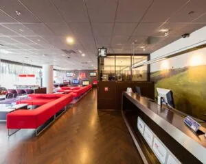 Moderne wachtruimte met rode banken en een receptiebalie, mogelijk in een zakelijke lounge of hotel.