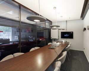 Moderne vergaderruimte met een lange houten tafel, designverlichting, een flatscreen en een flip-over.
