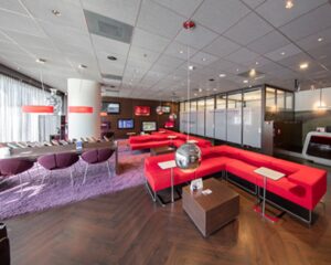 Moderne wachtruimte met rode zitbanken, paarse stoelen, leestafel en designverlichting.