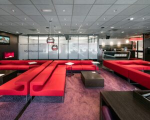 Moderne wachtruimte van NS International met rode banken, paarse vloerbedekking en glazen wanden.