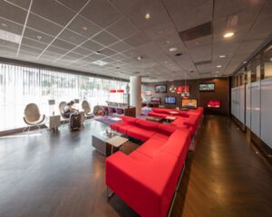 Moderne en ruim opgezette wachtruimte met rode banken, designstoelen en meerdere televisies aan de muur.