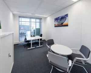 Modern ingerichte kantoorruimte met een bureau, vergadertafel en een grote foto van een satellietschotel aan de muur.