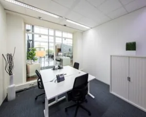 Moderne, lichte kantoorruimte met vier bureauplekken, telefoons en glazen wand met zicht op een ontvangstruimte.