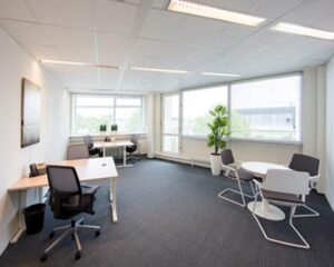 Licht en modern kantoor met meerdere bureaus, een ronde vergadertafel en grote ramen met uitzicht.