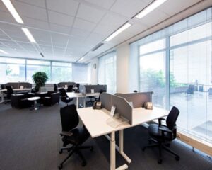 Moderne open kantoorruimte met bureaus, bureaustoelen en grote ramen die uitzicht bieden op een terras.