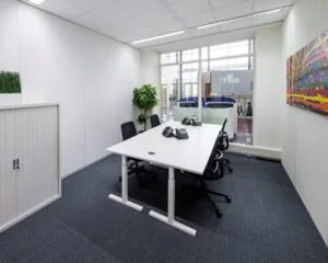 Moderne vergaderruimte bij Regus met een witte tafel, vier stoelen, telefoontoestellen en kleurrijk wandkunstwerk.