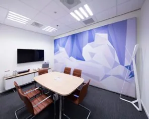 Vergaderruimte met zes bruine stoelen, een ovale tafel, een muurvullende abstracte muurschildering en een flatscreen tv.