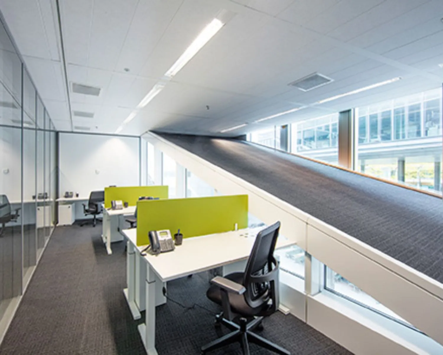 Modern kantoorinterieur met bureaus en opvallende schuine loopbandconstructie langs het raam.