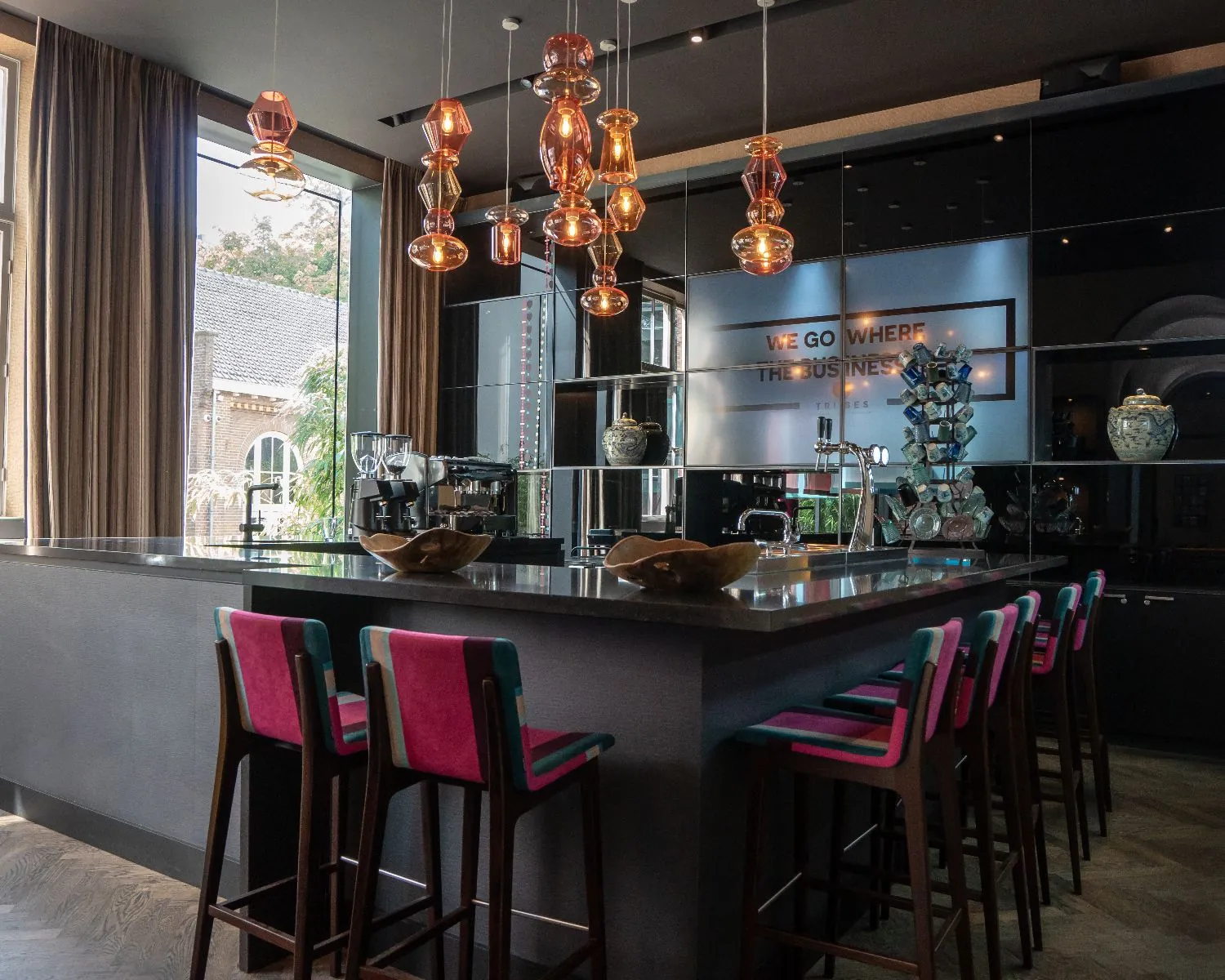 Moderne barruimte met hoogglans bar, kleurrijke barkrukken en artistieke hanglampen.