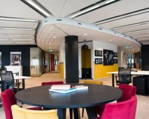 Moderne kantoorruimte met ronde vergadertafel, kleurrijke stoelen en open werkplekken.