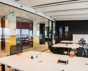 Moderne, open kantoorruimte met glazen wanden, witte bureaus en ergonomische bureaustoelen.