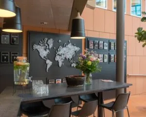 Kantoorruimte met een hoge tafel, bloemenvaas, watertap en een wereldkaart aan de muur.