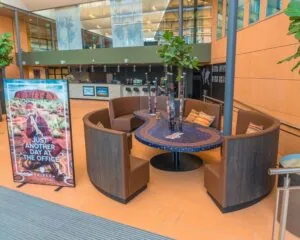 Moderne kantoorlobby met ronde zithoek, kleurrijke decoraties en een poster met de tekst "Just another day at the office" van Tribes.