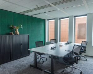 Modern ingerichte vergaderruimte met vier bureaustoelen, een grote tafel en een groene muur met een zwarte kast en decoraties.