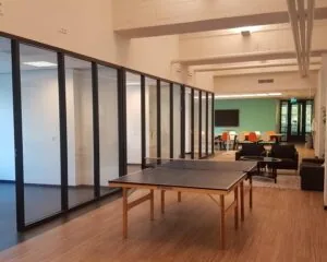 Moderne kantoorruimte met glazen vergaderruimtes, een tafeltennistafel, loungehoek en een vergadertafel met felgekleurde stoelen.