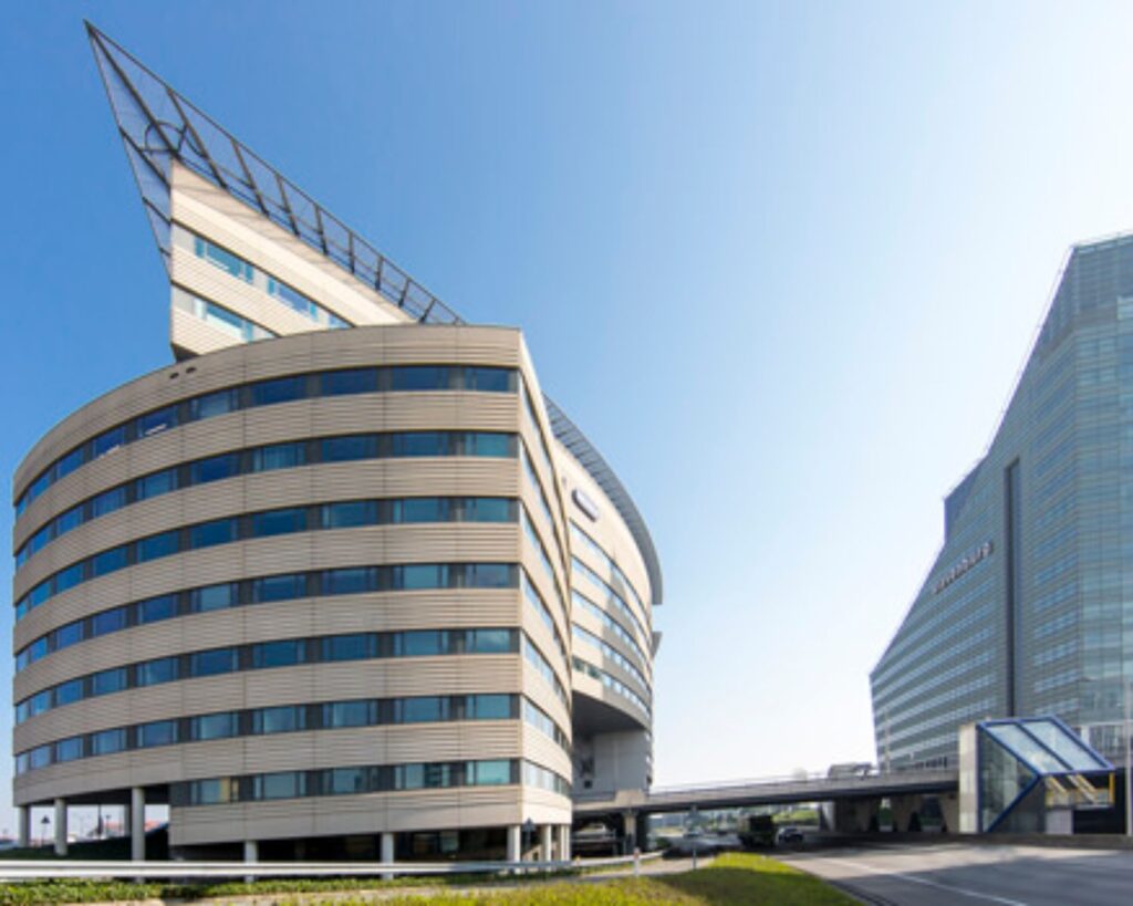 Kantoorgebouwen met moderne architectuur langs een weg onder een heldere blauwe lucht.