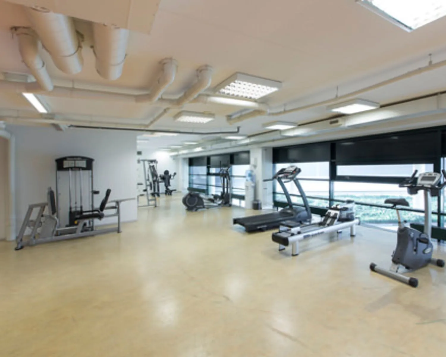 Ruime en moderne fitnessruimte met diverse cardio- en krachttoestellen en grote ramen.