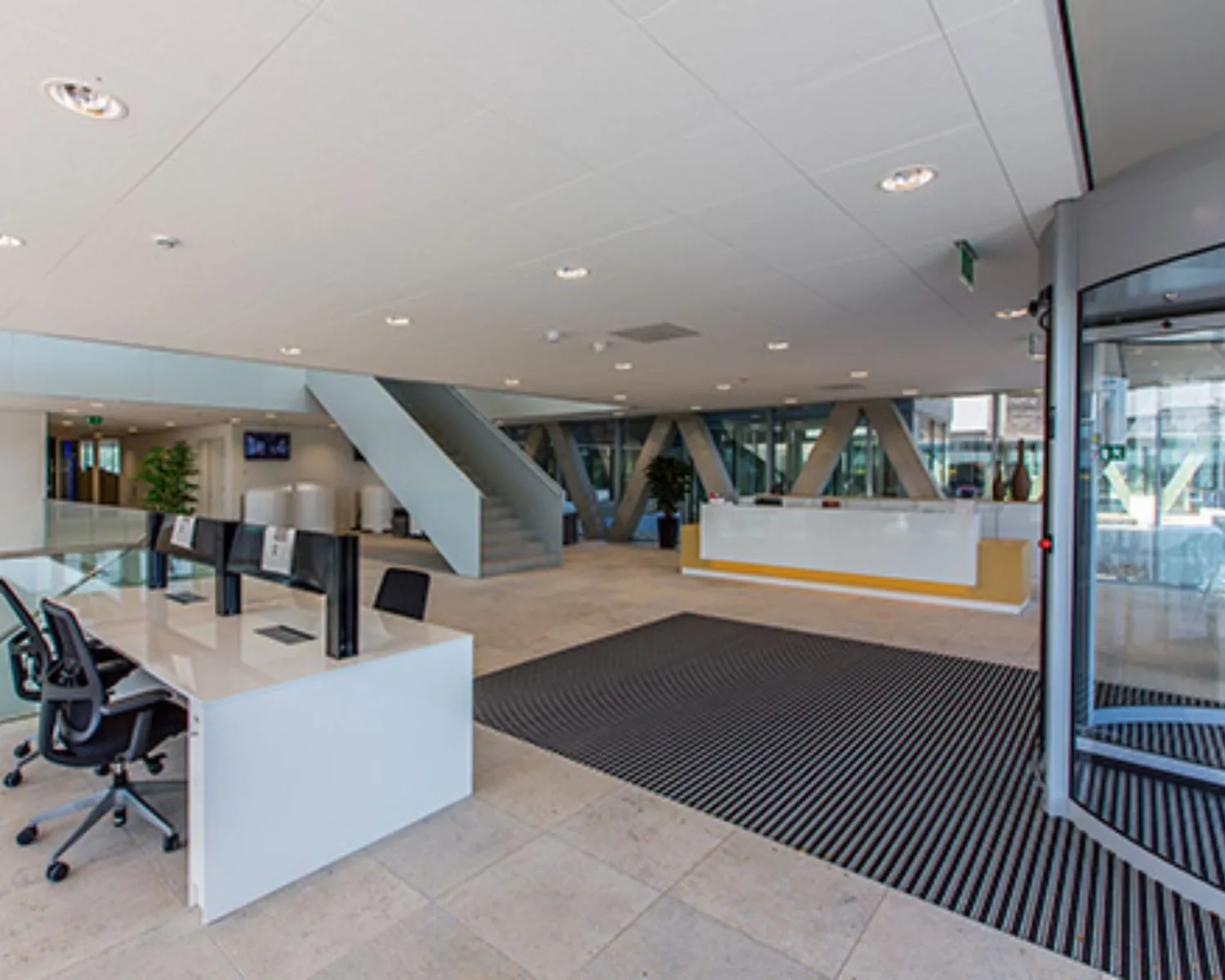 Moderne, lichte kantoorlobby met een receptiebalie, werkplekken en een glazen draaideur.