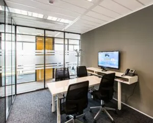 Moderne vergaderruimte met glazen wanden, vier stoelen, een witte tafel en een wandgemonteerde monitor.