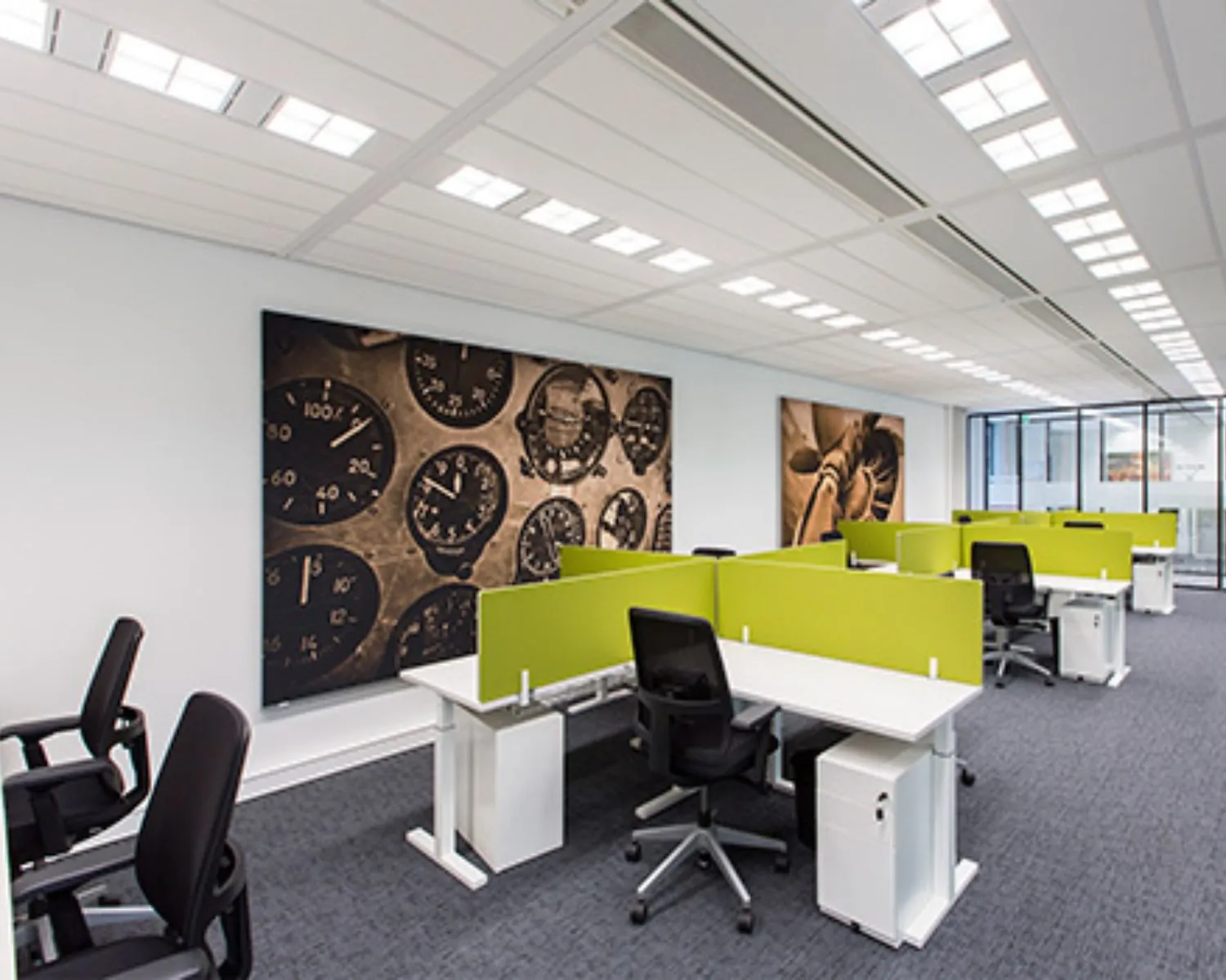 Modern kantoor met groene scheidingswanden, verstelbare bureaustoelen en grote wanddecoratie van instrumentenpanelen.