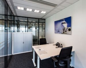 Modern kantoor met glazen wanden, twee bureaustoelen en een wandfoto van een vliegtuig.