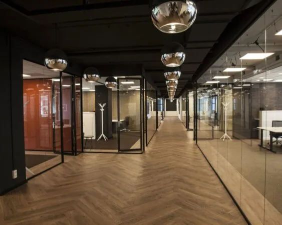 Moderne kantoorruimte met glazen wanden, houten visgraatvloer en spiegelende hanglampen.