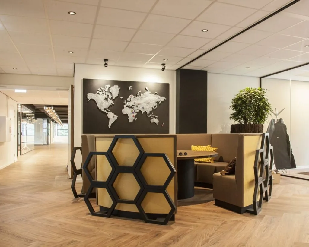 Moderne kantoorlounge met honingraatvormige stoelen, een ronde tafel en een wereldkaart aan de muur.