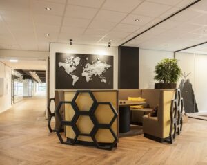 Moderne kantoorlounge met honingraatvormige stoelen, een ronde tafel en een wereldkaart aan de muur.