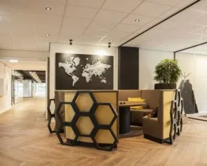 Moderne kantoorlounge met honingraatvormige stoelen, een ronde tafel en een wereldkaart aan de muur.