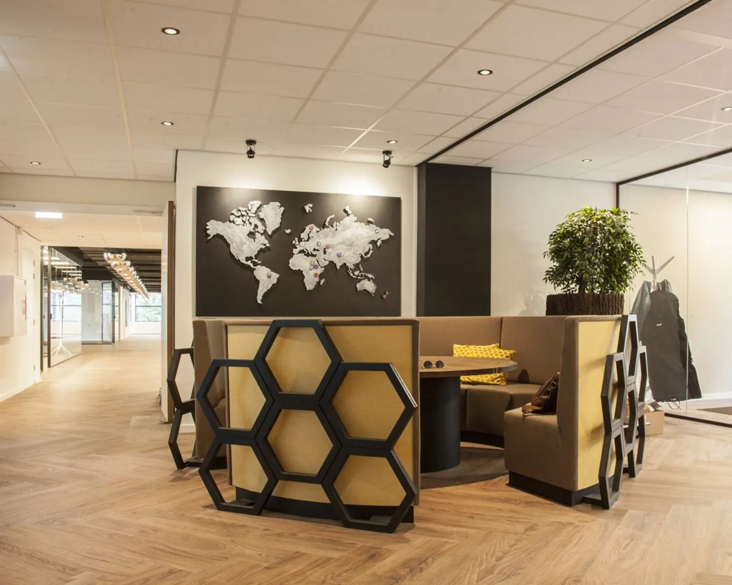 Moderne kantoorlounge met honingraatvormige stoelen, een ronde tafel en een wereldkaart aan de muur.