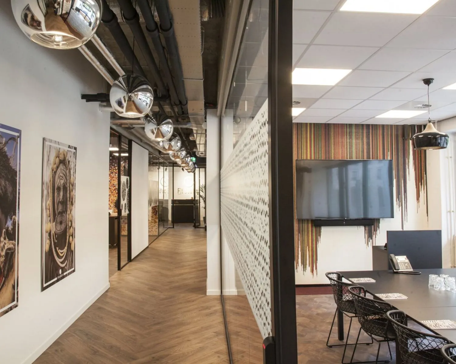 Modern kantoorinterieur met glazen vergaderruimte, houten vloer en wanddecoratie met kleurrijke strepen.