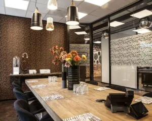 Moderne vergaderruimte met houten tafel, zwarte stoelen, hanglampen en bloemenvaas als middelpunt.