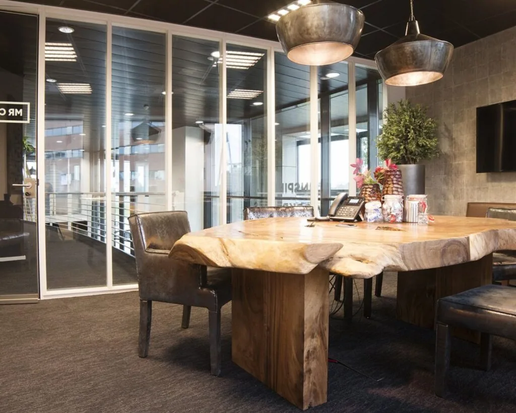 Vergaderruimte met een robuuste houten tafel, leren stoelen en industriële hanglampen.