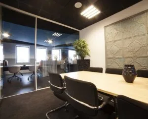 Moderne vergaderruimte met zwarte stoelen, houten tafel, glazen wand en decoratieve elementen zoals een plant en een reliëfmuur.