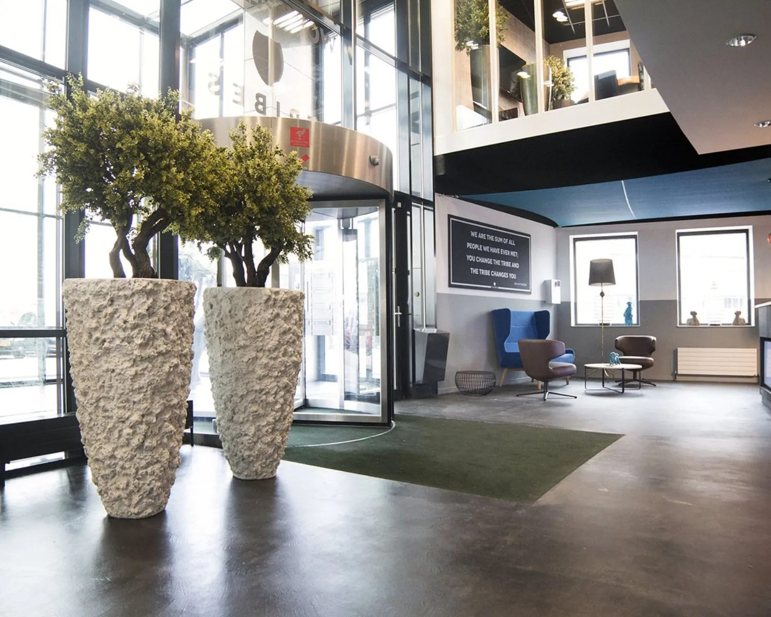 Moderne kantoorentree met grote plantenbakken, draaideur en een stijlvolle wachtruimte met zitmeubels.