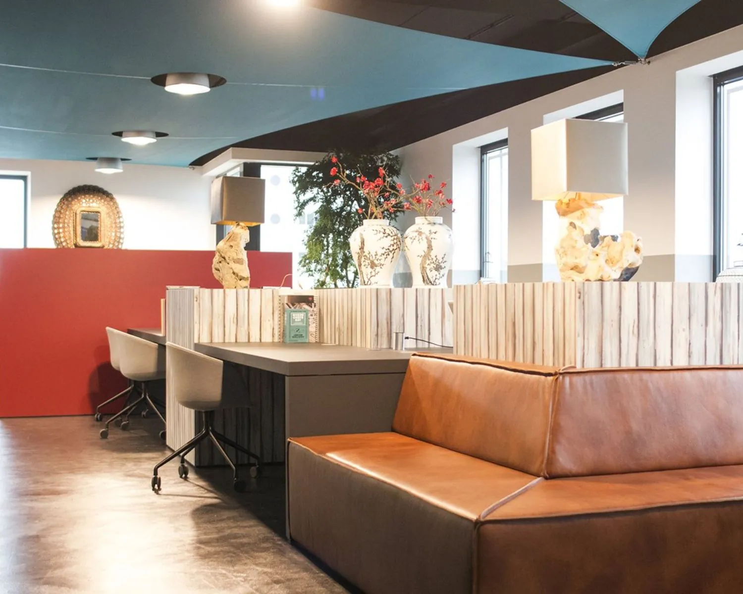 Modern ingerichte kantoorruimte met leren zithoek, werkplekken, decoratieve vazen en zacht plafondlicht.